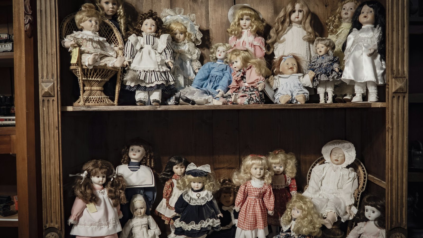 Wooden cabinet shelves crowded with antique-style porcelain dolls in lace and gingham dresses