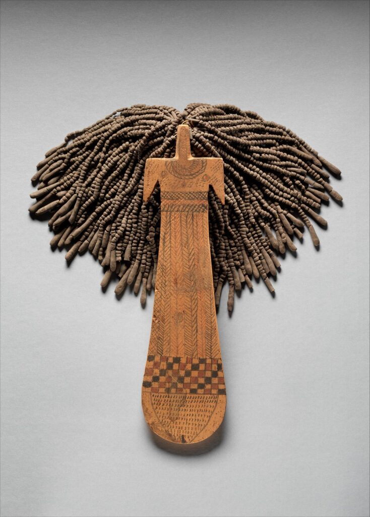 Flat wooden Egyptian paddle doll with painted patterns and a thick fringe of strung mud-bead hair