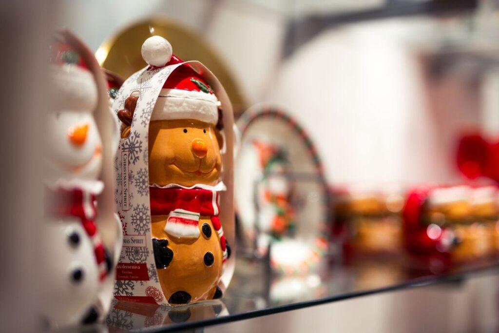 Glossy glazed ceramic Christmas bear decoration in a Santa hat and red scarf on a glass shop shelf