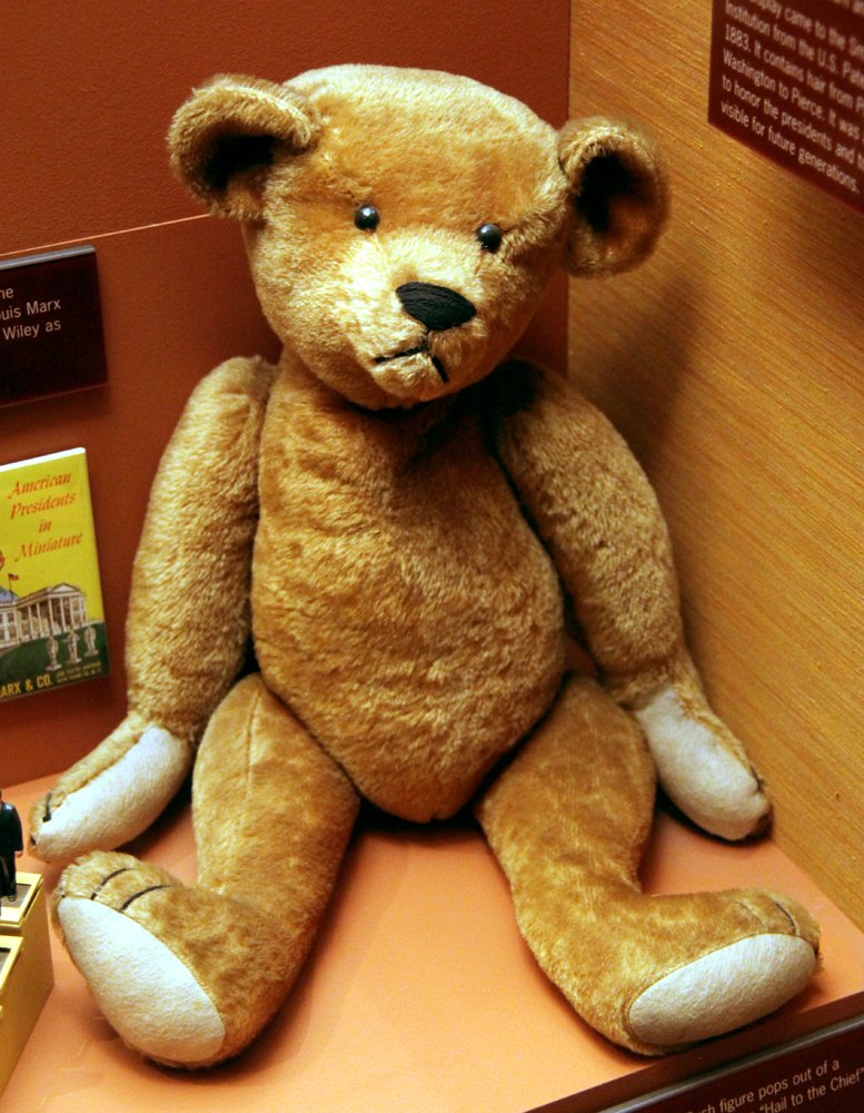 Golden mohair teddy bear made by the Ideal Toy Company around 1903, seated in a museum display case
