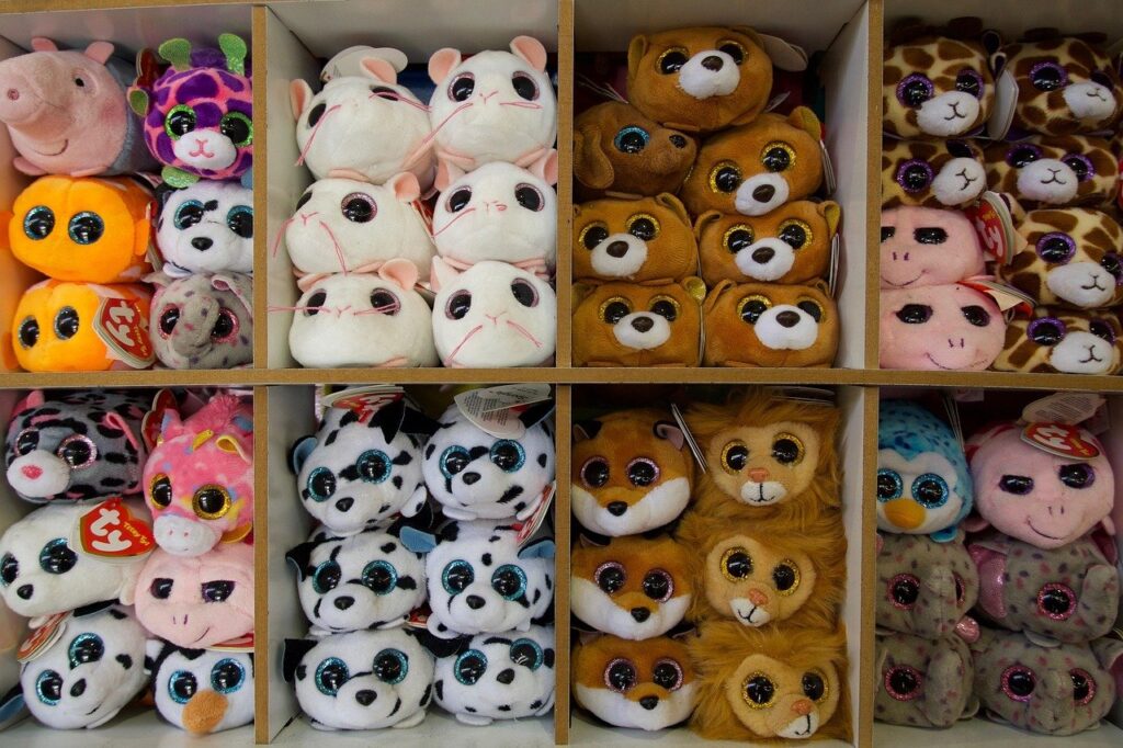 Rows of small big-eyed plush animals on a store shelf, many with red heart-shaped hang tags