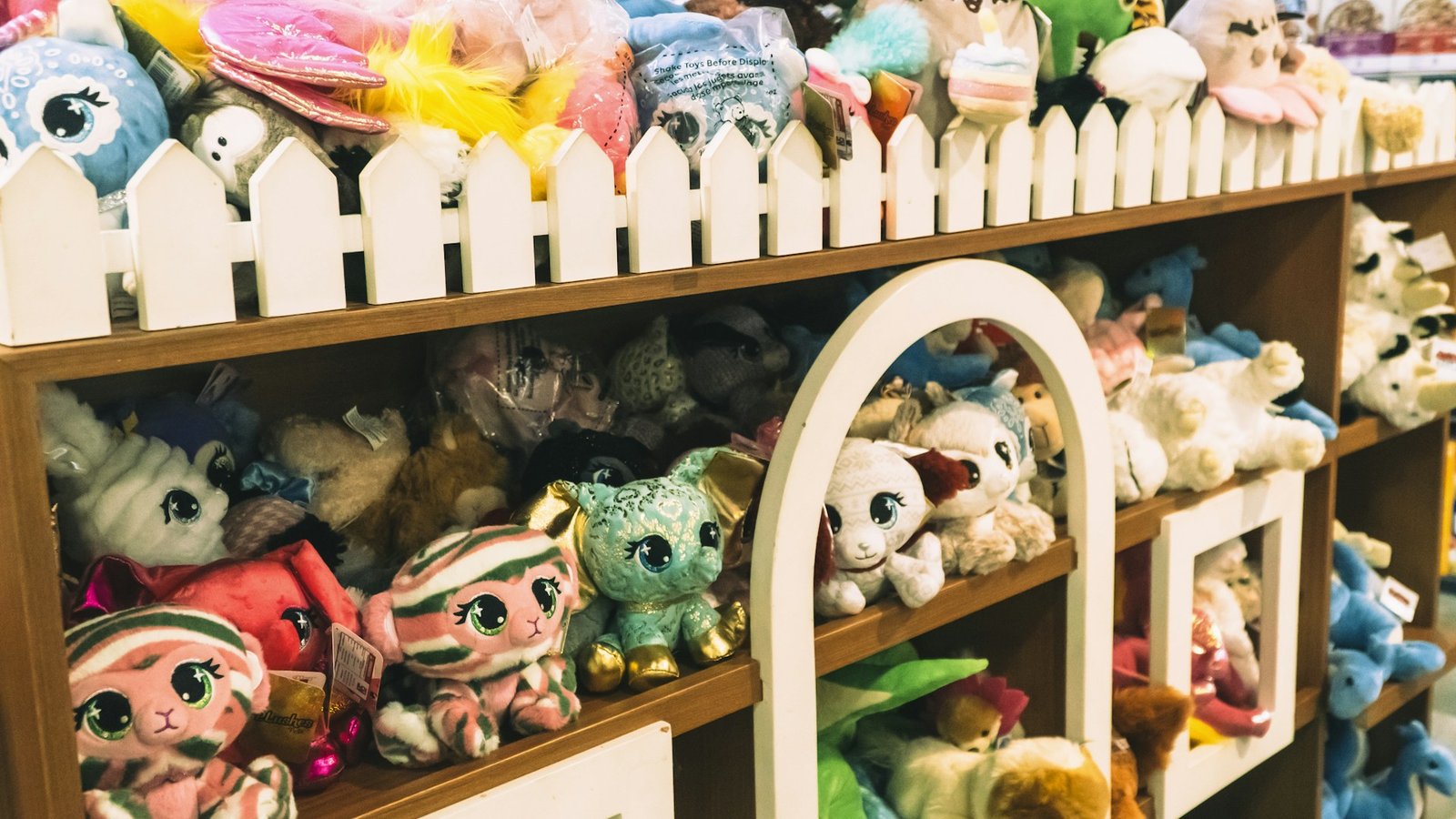 Shelves in a toy shop packed with colorful plush animals behind a small white picket fence display