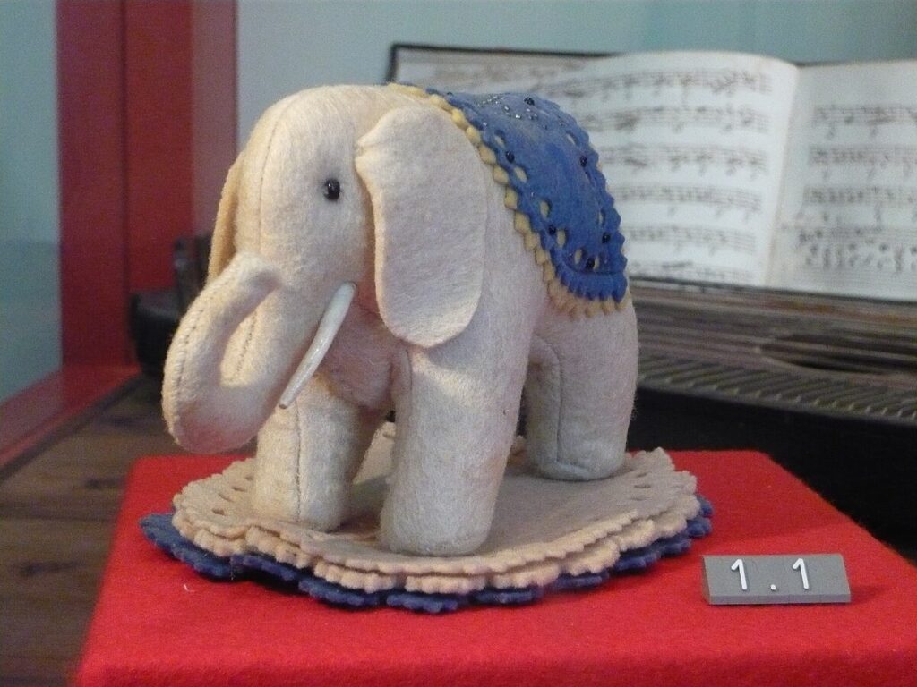 Small cream felt elephant pincushion with a blue saddle cloth, displayed at the Steiff Museum in Giengen
