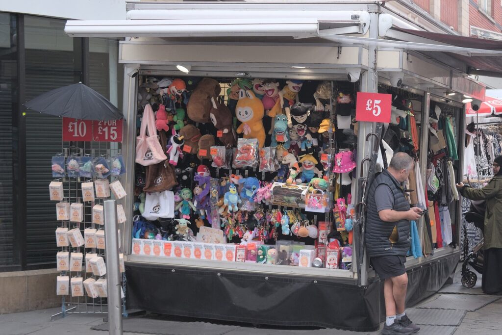 Market stall in Nottingham hung with plush toys and bag charms, with price signs for 5 and 10 pounds