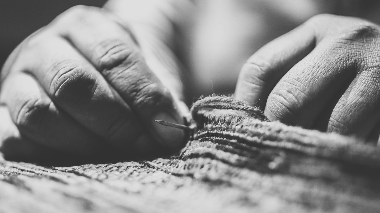Black-and-white close-up of a person hand-sewing a thick fabric with a needle and thread